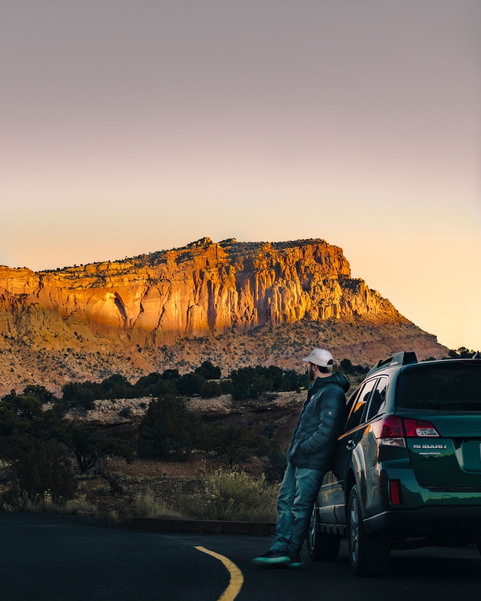 man leaning on green vehicle waiting for roadside assistance
